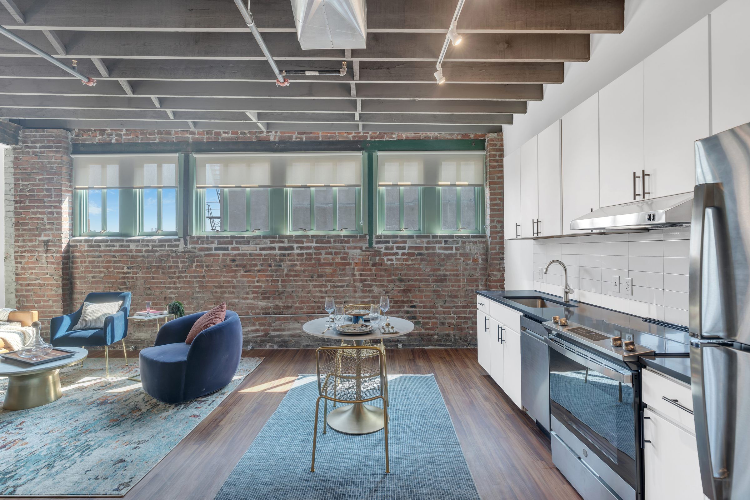 West Bottoms Flats apartment living room with open floor plan and urban core features like raft ceilings, brick walls, large windows and modern furniture