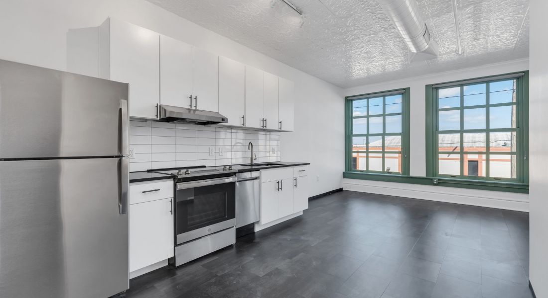 West Bottoms Flats apartment living room with dark wood tile floors and modern kitchen juxtaposed with large historic windows