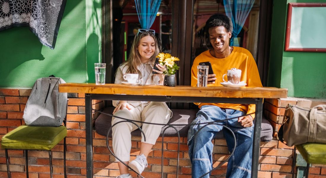 Two young adult friends sitting at an outside bar in front of a funky coffee shop