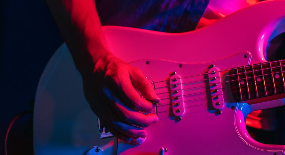 Close-up of man playing an electric guitar under fuchsia lights