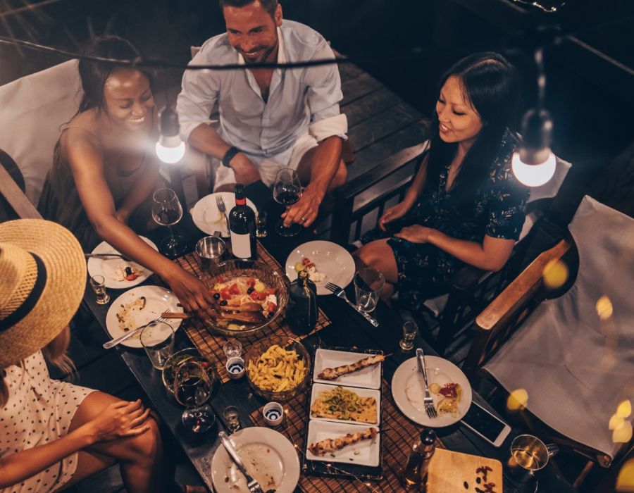 Group of friends having dinner out at night under string lights sharing many plates of food