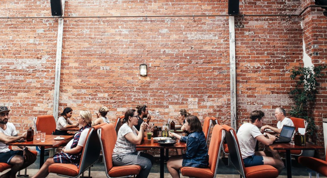 People eating inside of a busy restaurant with brick walls and high ceilings